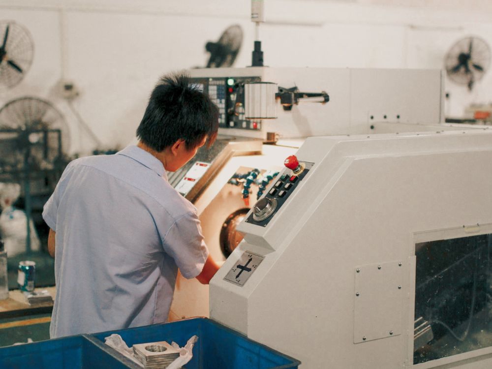 Operador industrial ajustando máquina CNC em ambiente fabril, realizando usinagem de peças metálicas com painel de controle automatizado.