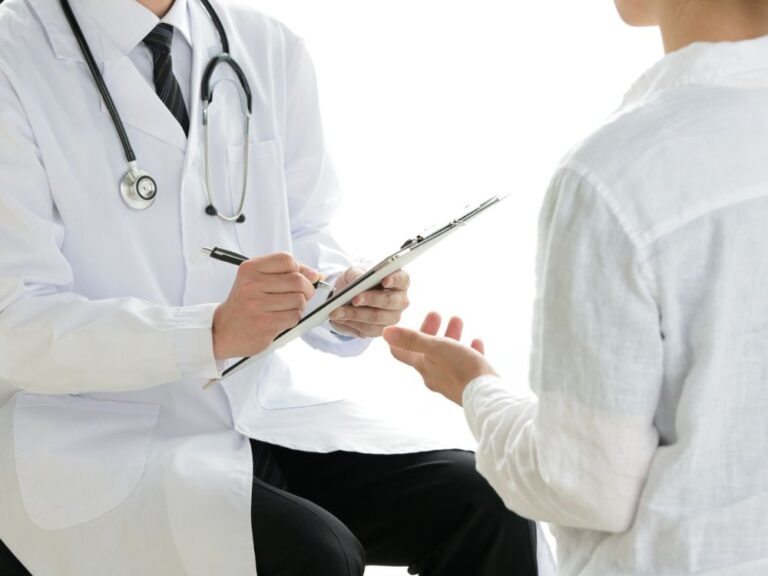 Médico realizando atendimento com paciente, anotando informações em prancheta durante consulta clínica para diagnóstico.